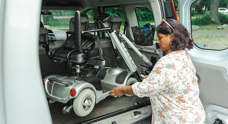 Hilary lastar in sin elektriska scooter i bilens bagageutrymme med hjälp av en rullstolskran.